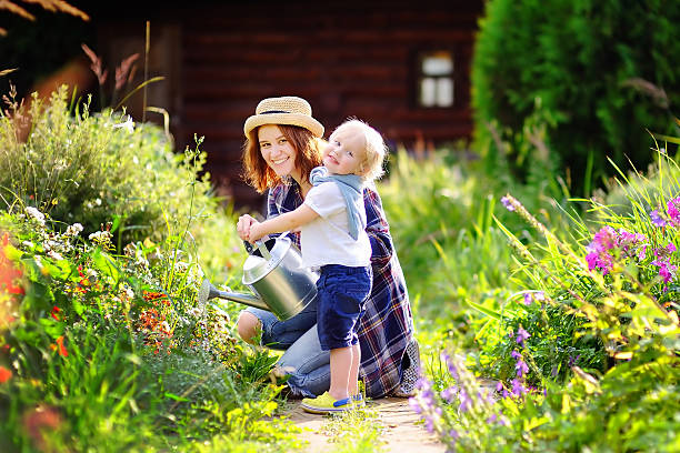 Cute toddler boy and his young mother watering plants in the garden at summer sunny day